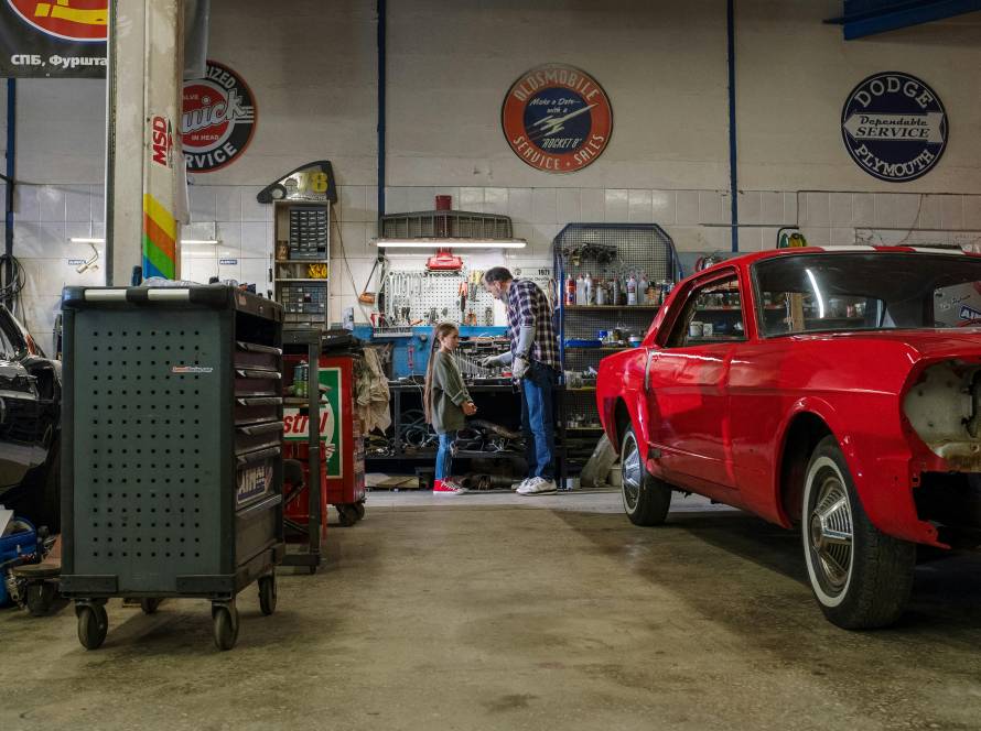 Grandfather and Granddaughter working in a car garage with red car